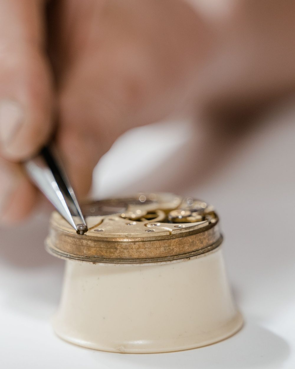 Tweezers lifting a tiny screw from a brass movement resting on a movement holder.