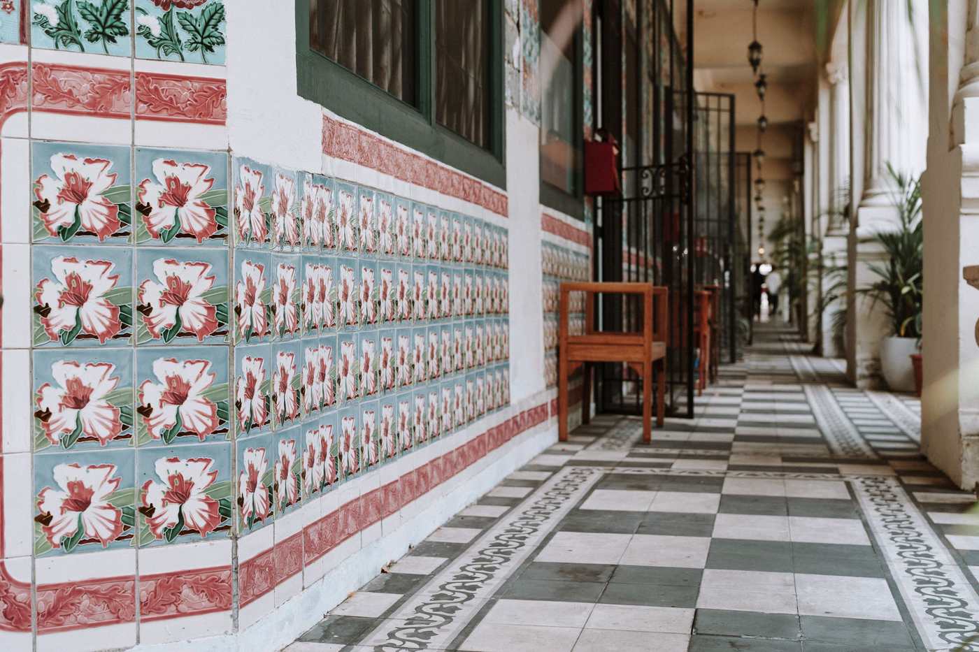 A covered five-foot way lined with hand-painted floral tiles in pink and green, with a chequered floor running into the distance.