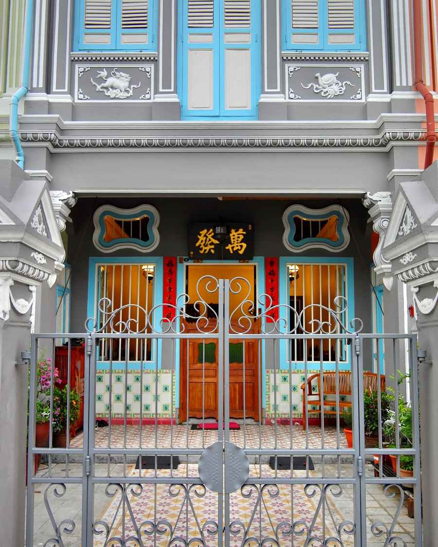 A Joo Chiat shophouse front with turquoise shutters, carved plaster and an ornate iron gate.