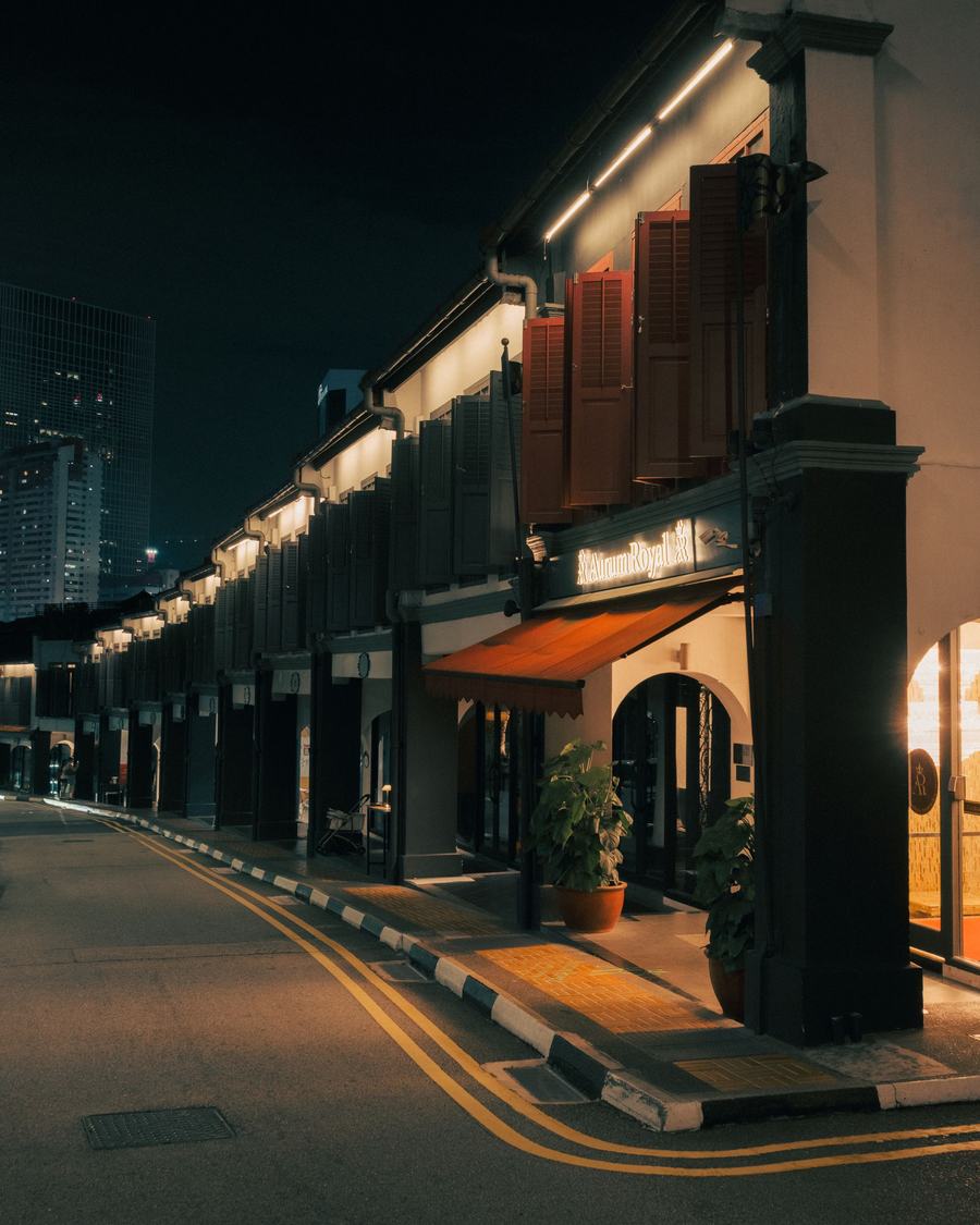 A row of shophouses at night, warm light spilling from the arches onto an empty street.