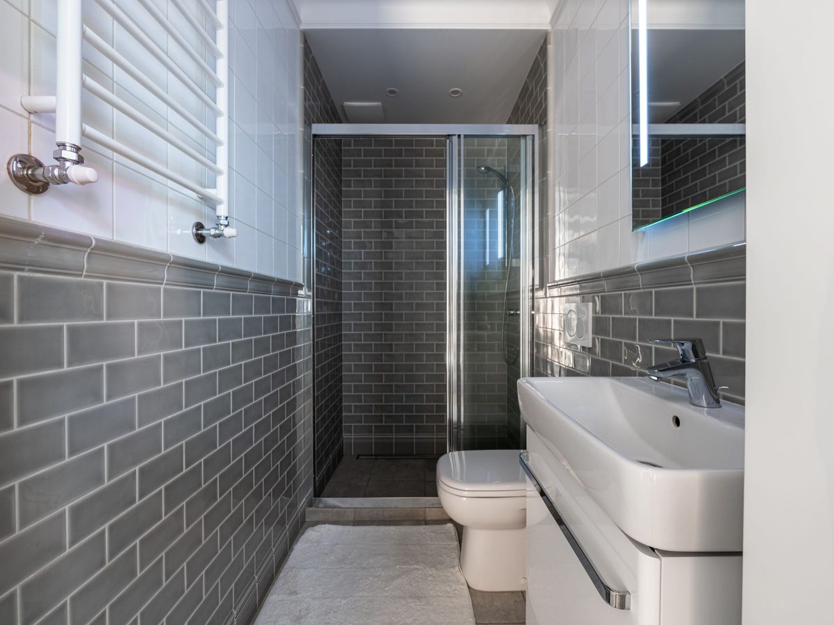After: a compact bathroom with grey subway tiles, a glass shower screen and a wall-hung basin.