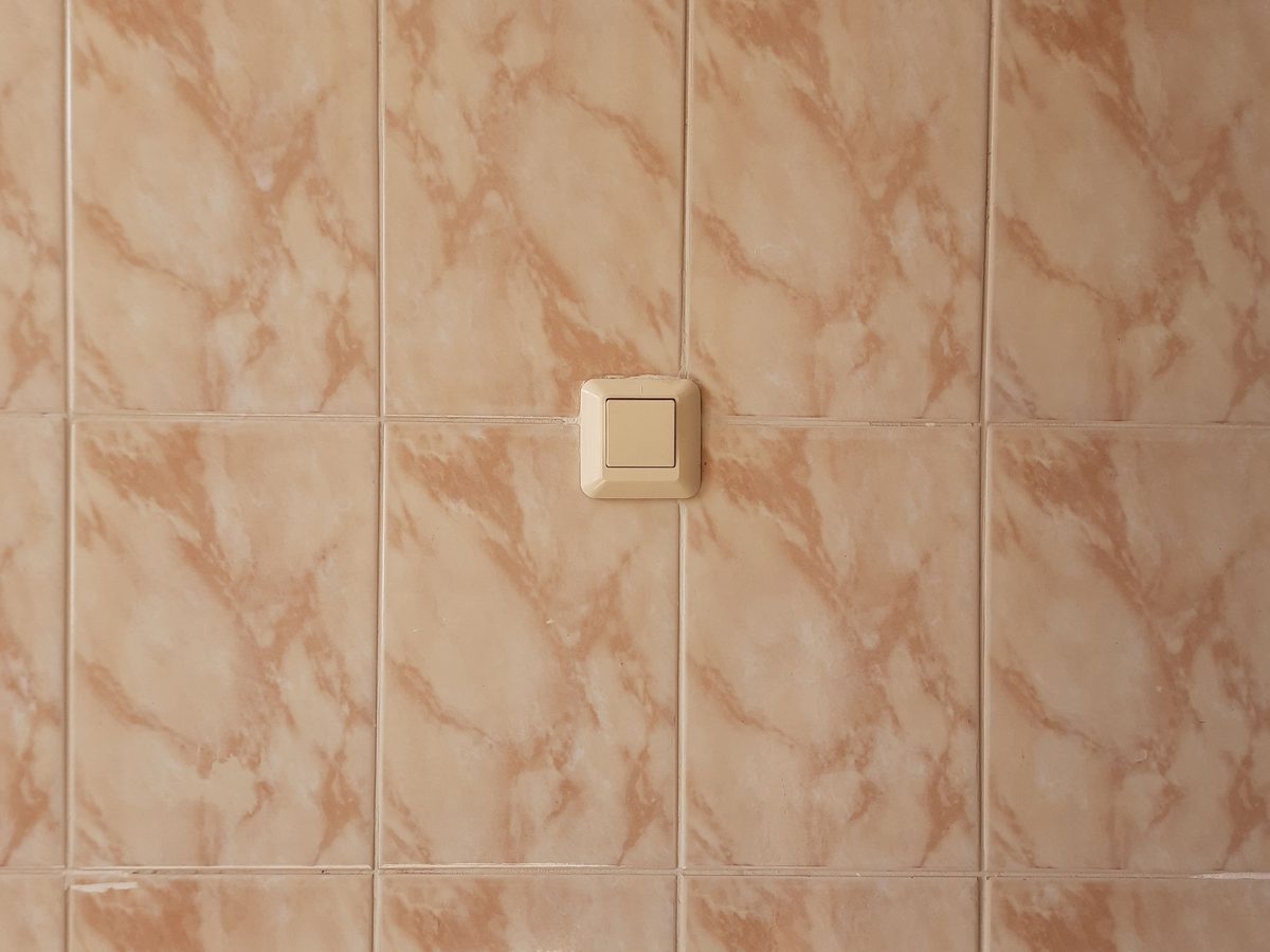 Before: dated pink marble-effect wall tiles with an old light switch.