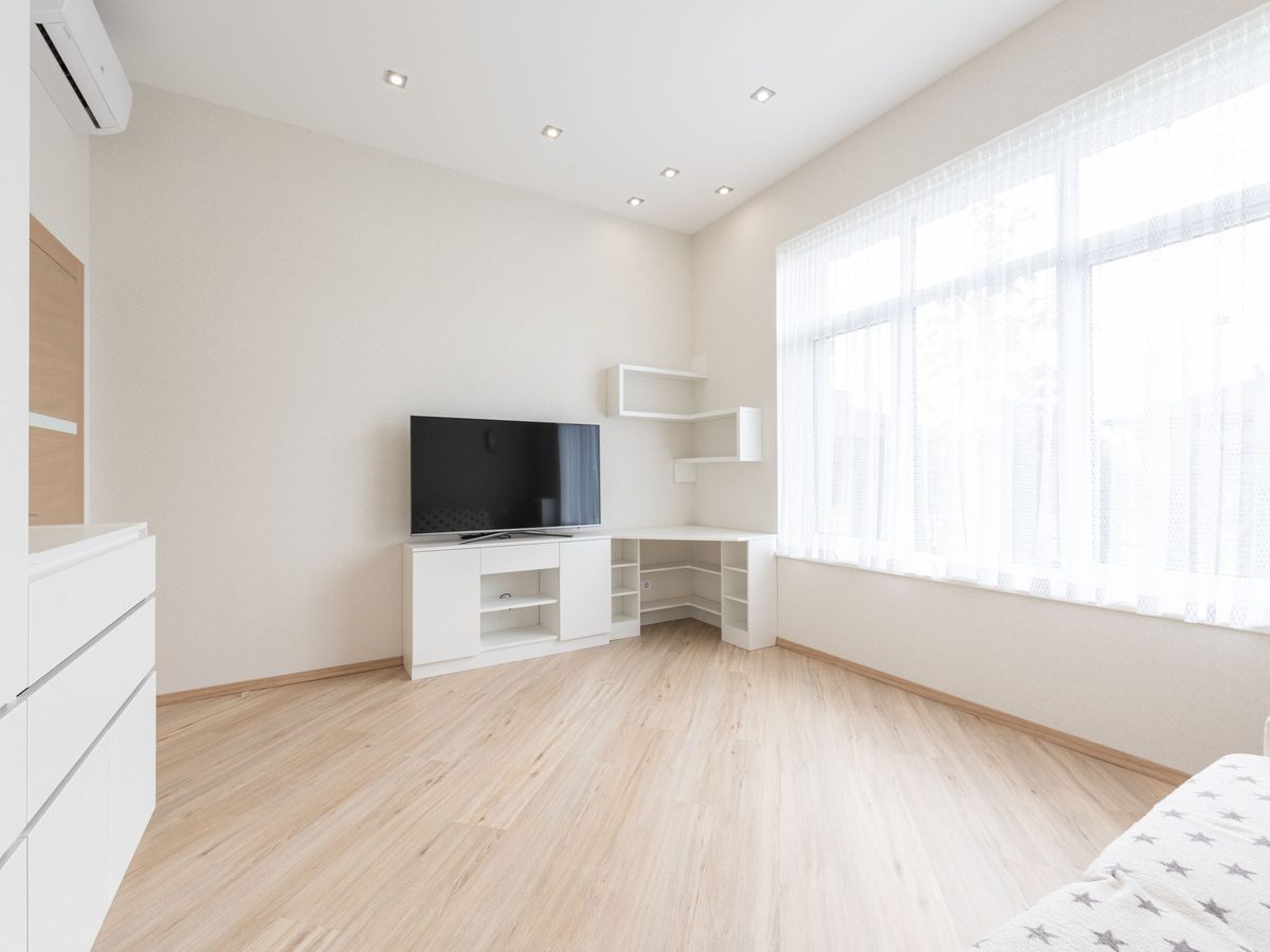 After: a bright living room with light vinyl flooring, white built-in shelving and a wall-mounted TV.
