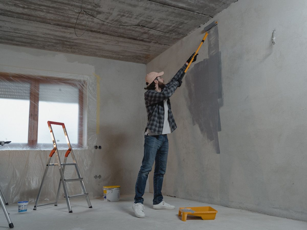 Before: a bare grey room with an unfinished ceiling, a worker painting the wall and a stepladder.