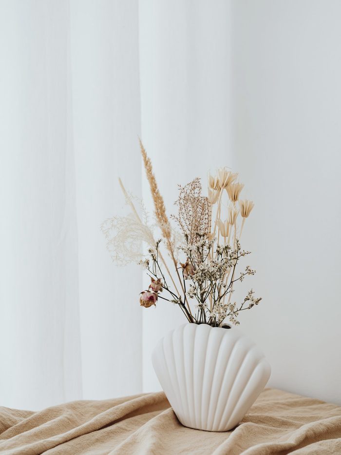Dried pampas, bunny tails and wheat-coloured grasses in a white scalloped ceramic vase on linen.