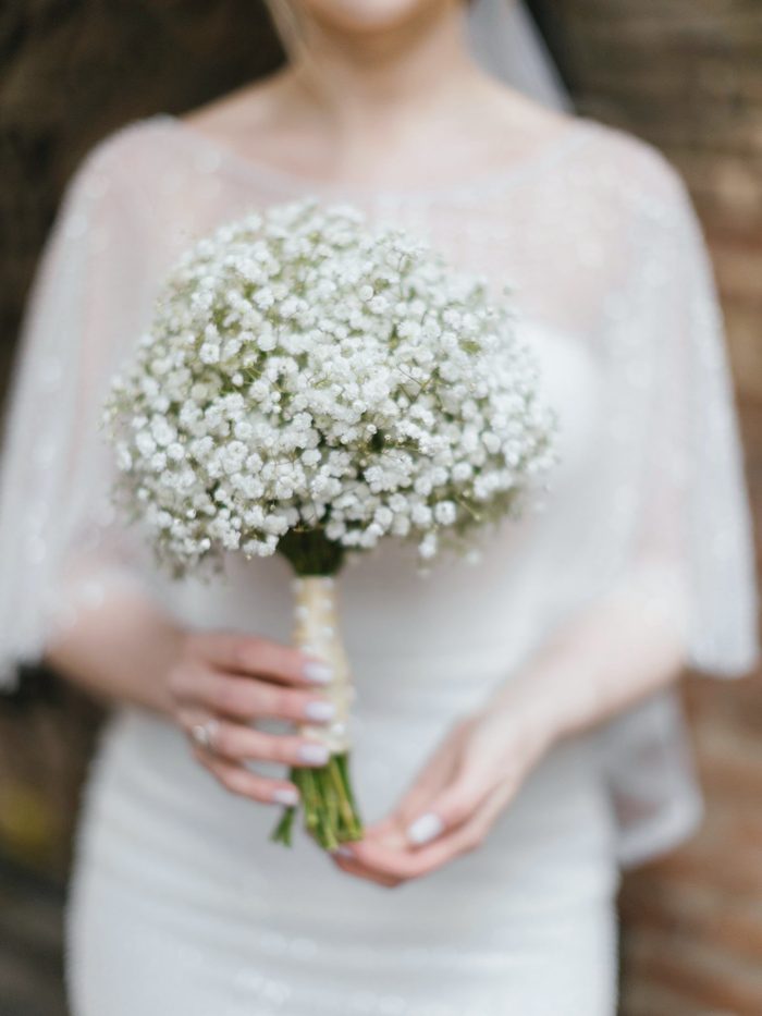 A bride holding a round, dense bouquet of white baby's breath with a ribbon-wrapped stem.
